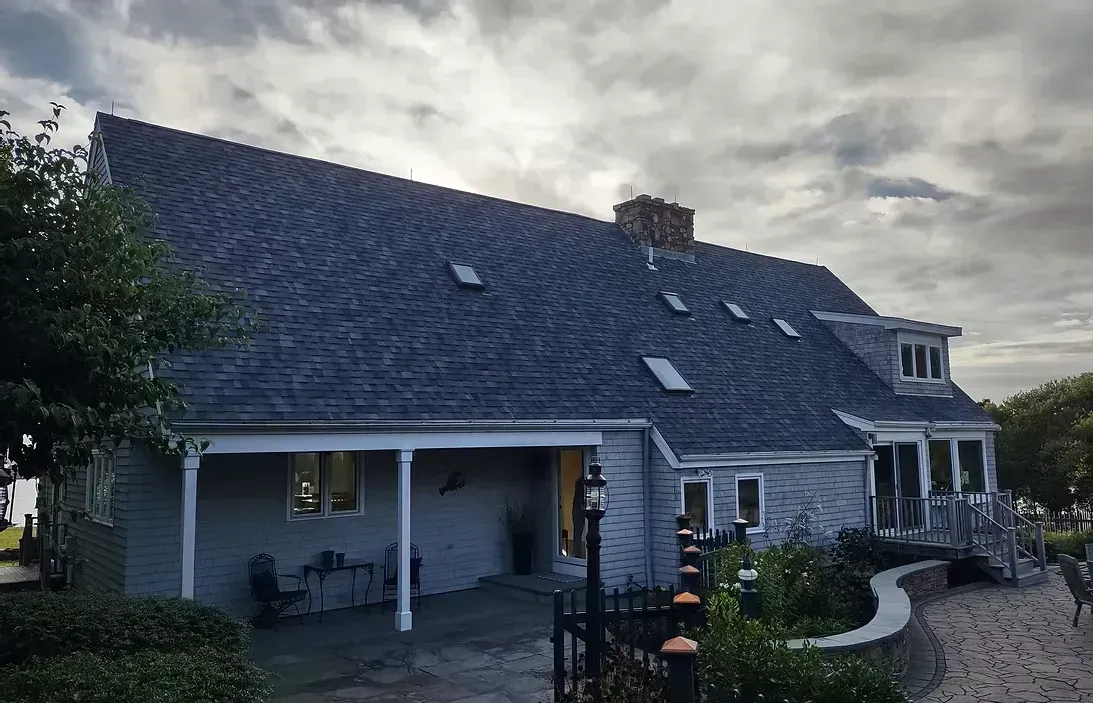 Gray house with a dark, patterned roof, porch, and a cloudy sky.