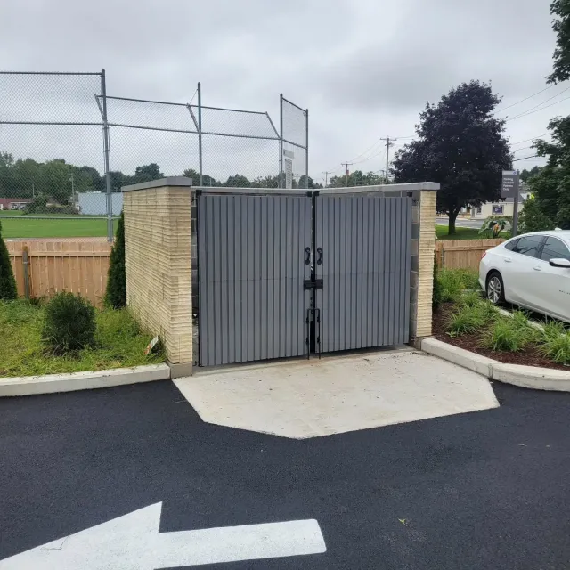 Gray trash enclosure with concrete pad and arrow on pavement.