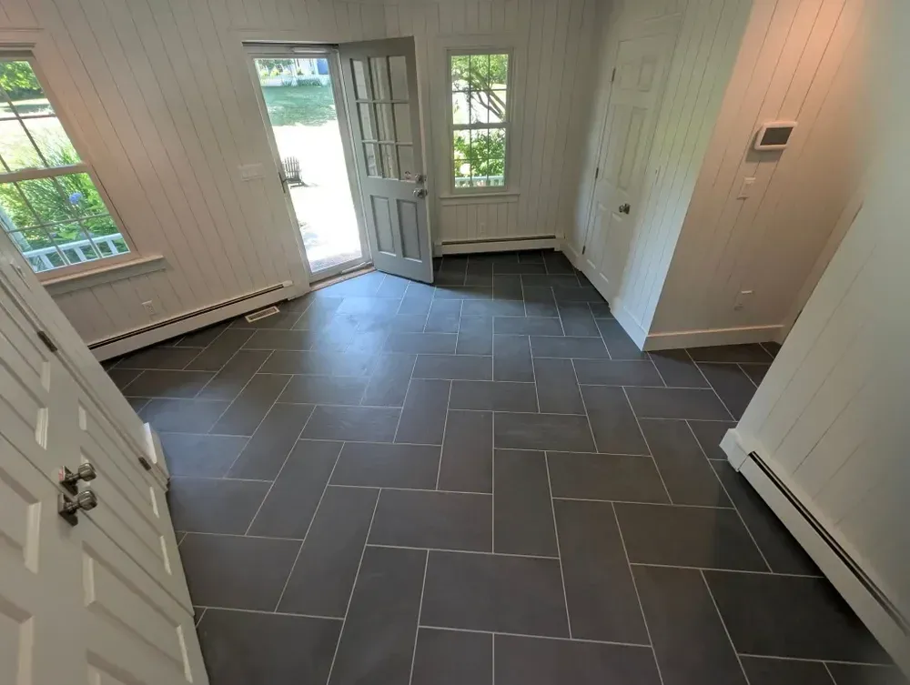 Empty room with dark gray tiled floor, white paneled walls, and open door leading outside to greenery and water. Windows with views of trees and a deck area.