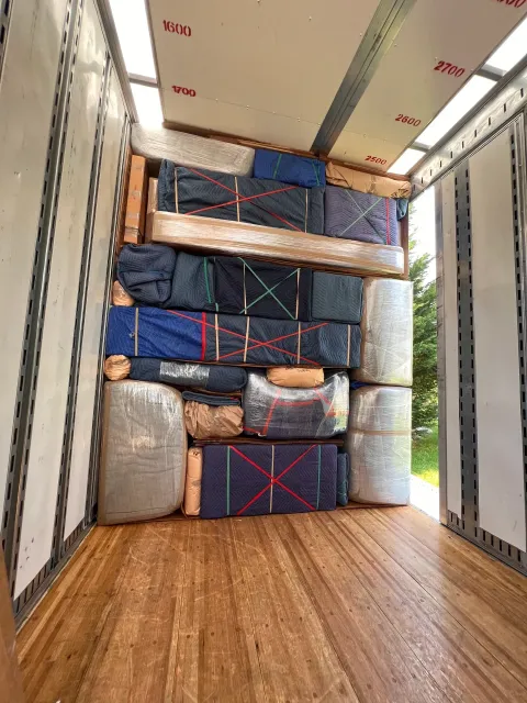Packed moving truck with stacked mattresses and furniture blocking the cargo area and wooden floor