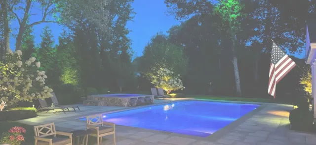 A large swimming pool is lit up at night in a backyard.
