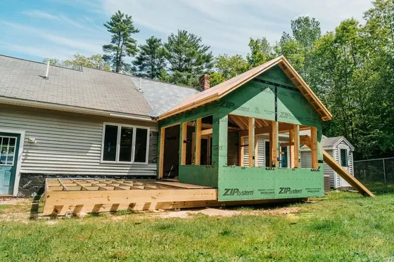 House with partially built green porch addition and wooden steps in a grassy yard