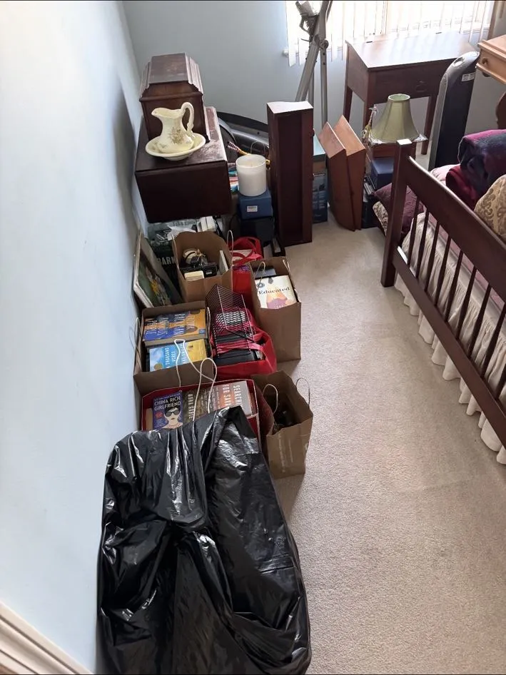 Same bedroom before, lined with boxes, bags and stacked furniture