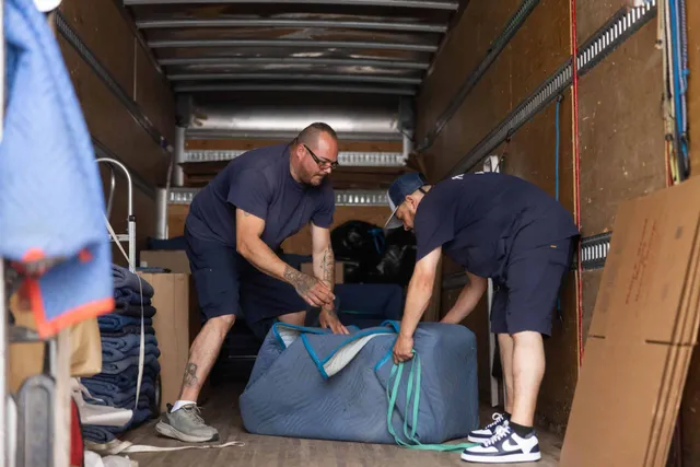 Two men unloading a large piece of furniture from a moving truck.
