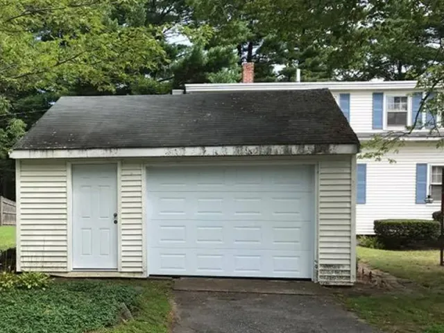 A white garage with a black roof is in front of a white house.