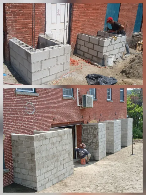 Construction worker building concrete block walls outside a brick building.