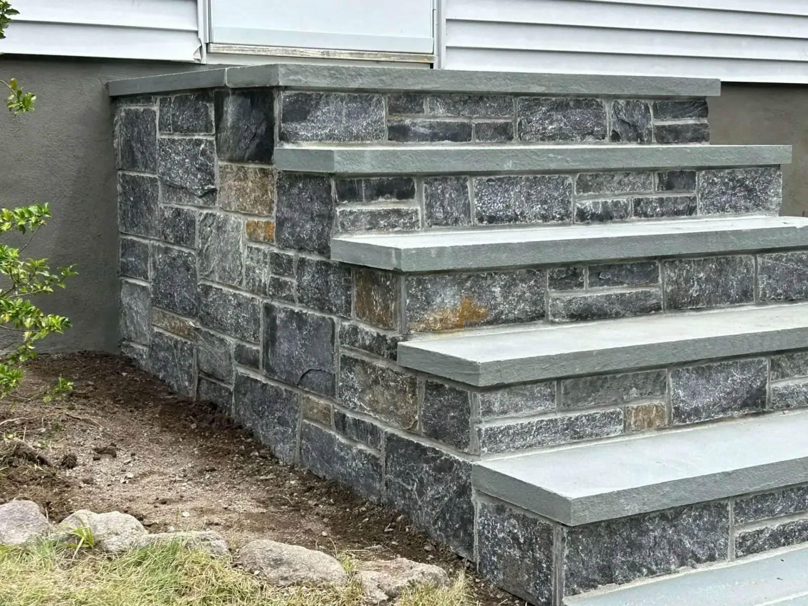 Stone steps leading up to a white house with gray stone facing.