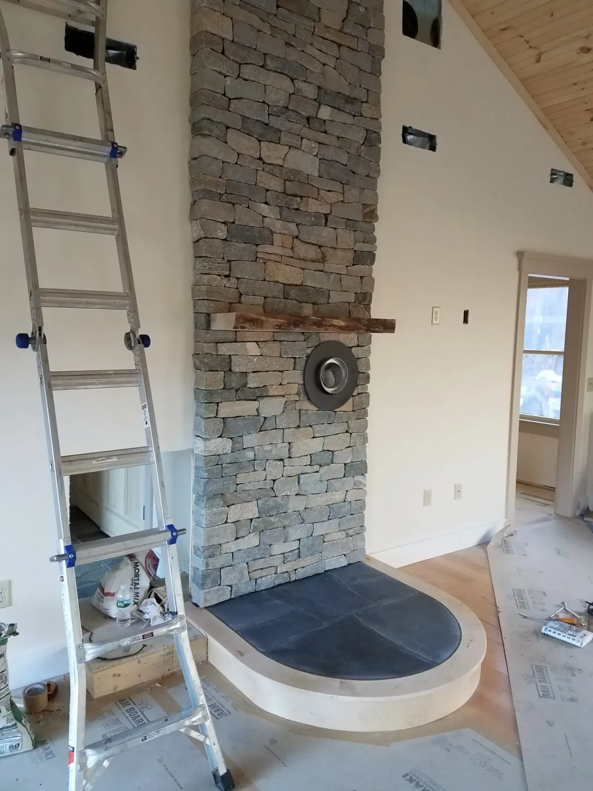 Ladder leaning against a stone fireplace under construction. The hearth has a curved border.