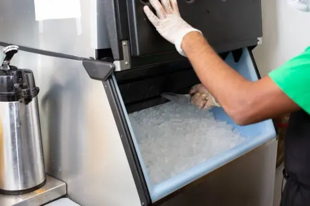 A person is cleaning an ice machine in a kitchen.
