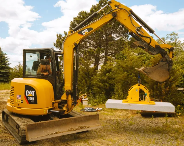 Granite step being moved with a mini-excavator and a pneumatic lifter.