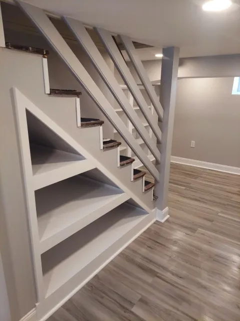 Partially constructed staircase with a bookshelf underneath, white painted walls, wood flooring, and a small window in a modern interior.