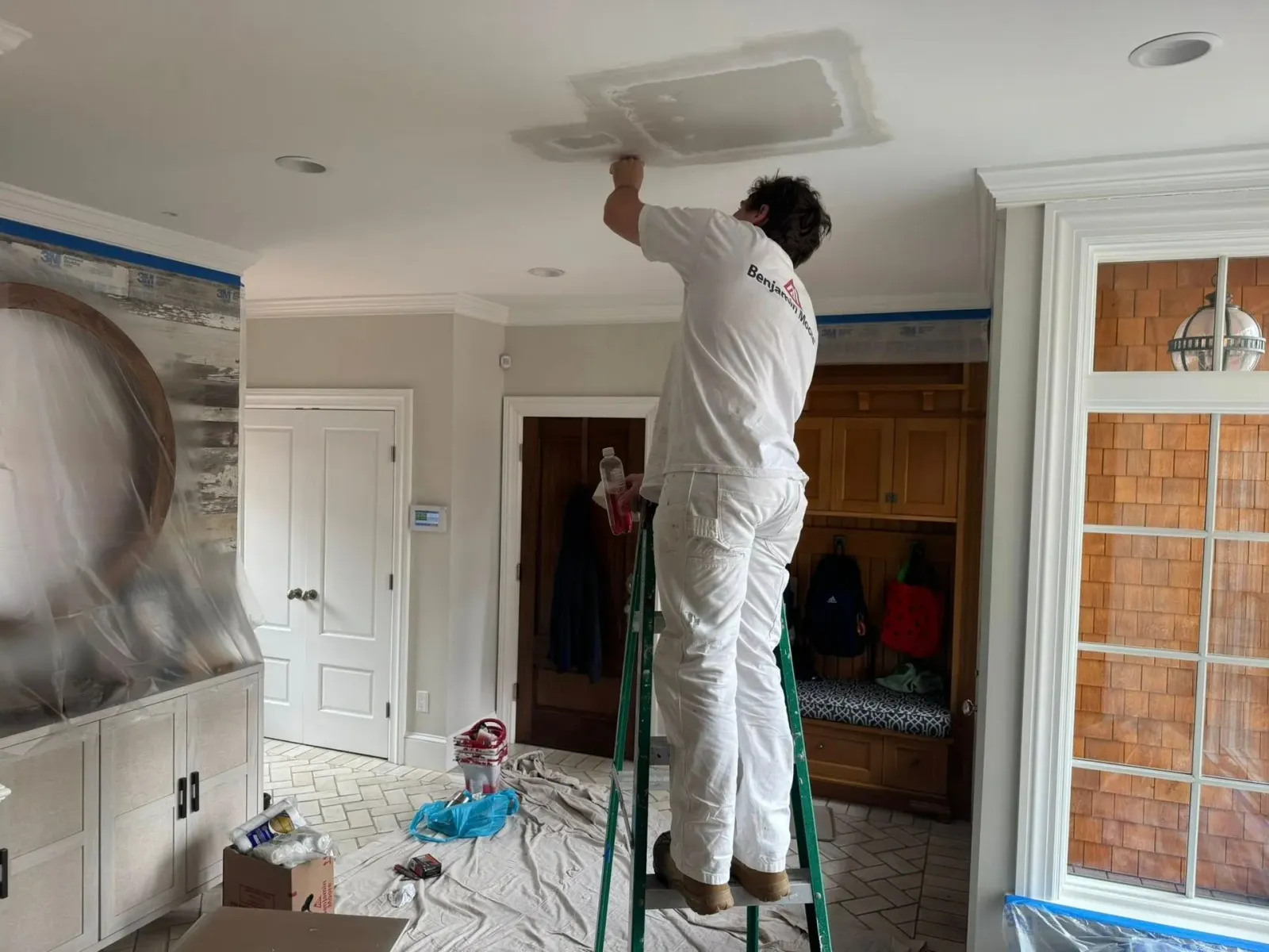 Person painting a ceiling vent in a room with drop cloths and a ladder