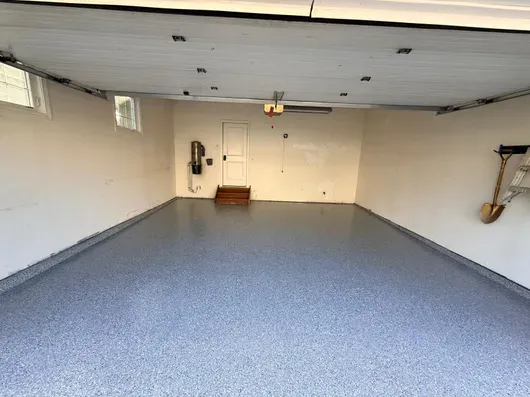 Empty garage interior with gray speckled floor, white walls, and closed door at the far end