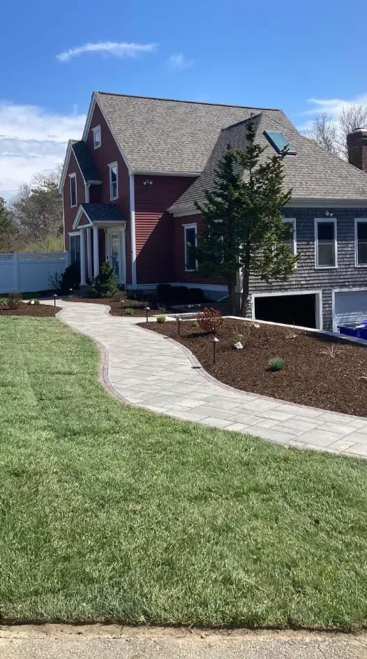 Two-story house with a paver walkway, landscaped yard, and grass. Red and blue exterior with blue sky.