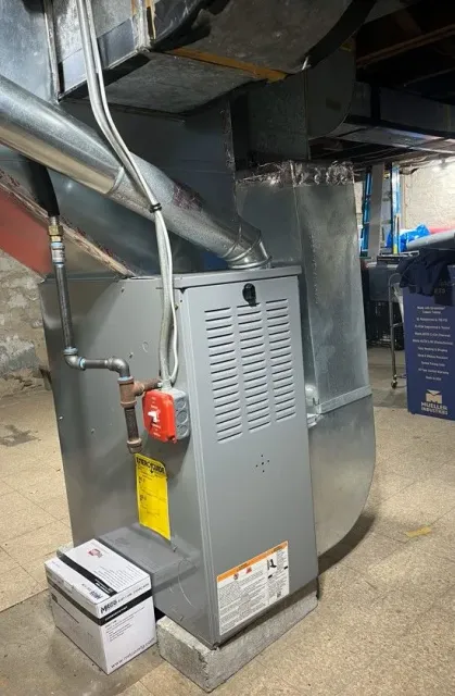 A furnace is sitting in a basement next to a box of batteries.