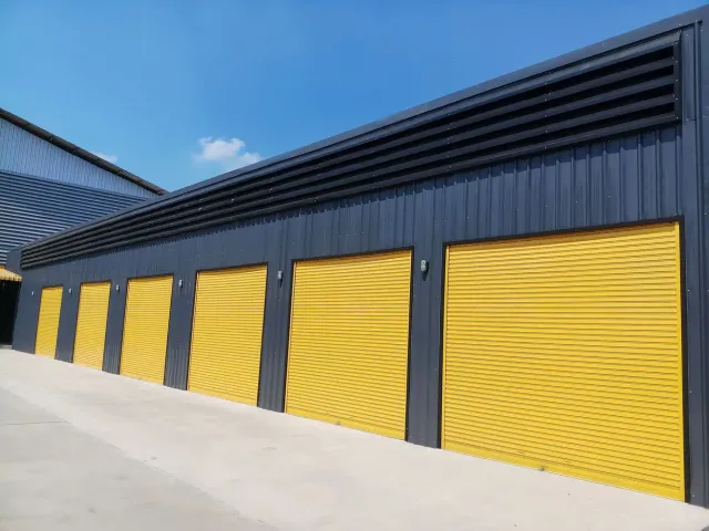 Industrial building with yellow garage doors and dark siding under a blue sky