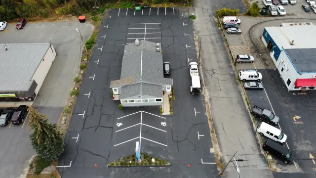 Aerial view of a commercial building with a surrounding asphalt parking lot containing marked spaces and vehicles.