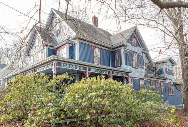 A large blue house with red-rimmed windows as seen from a street view.