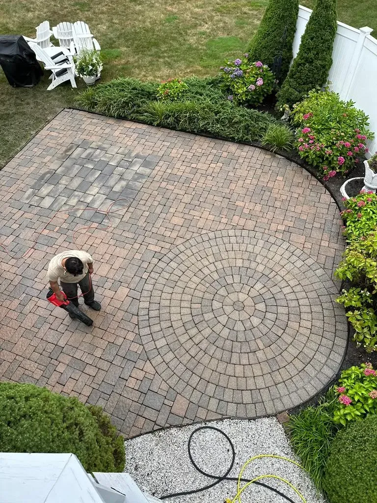 Person pressure washing a brick patio in a backyard.