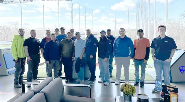 A group of people standing on a golf course patio, smiling.
