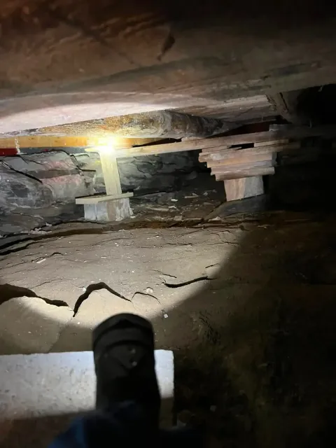 Flashlight illuminating a narrow crawlspace with rough beams and debris on the ground