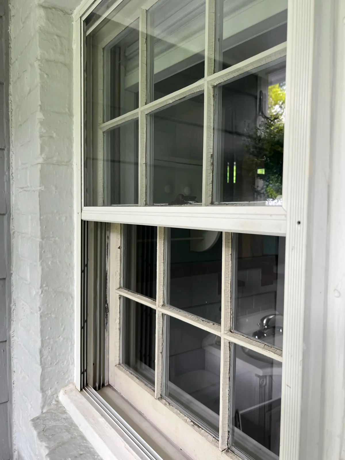 Close-up of a window with wooden grid panes, showing a sink and some interior elements visible through the glass.