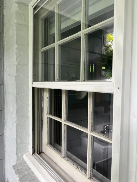 Close-up of a window with wooden grid panes, showing a sink and some interior elements visible through the glass.