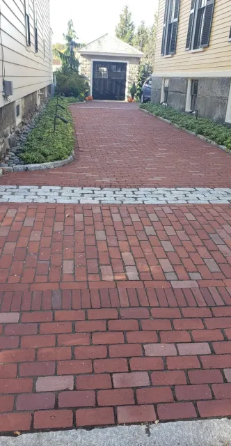 A brick walkway with a sidewalk and plants.