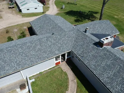 Aerial view of a gray-shingled house with a red door and grassy courtyard