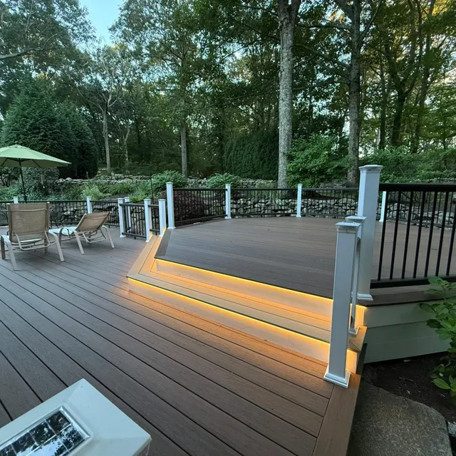 Custom composite deck at dusk showcasing warm under-step LED lighting and white railing posts.