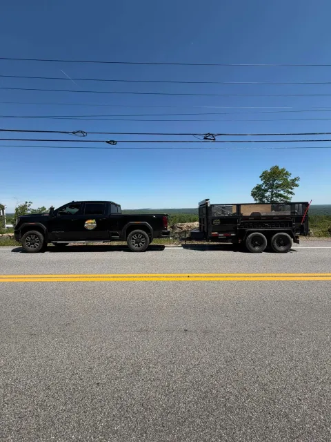Black pickup truck towing a small trailer on a roadside under a clear blue sky.