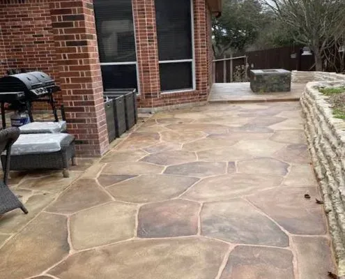 Stone-patterned concrete patio with a brick house and built-in fire pit.