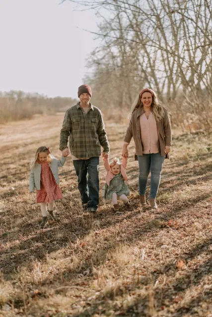 Family walking outdoors in a park during autumn, smiling and holding hands.