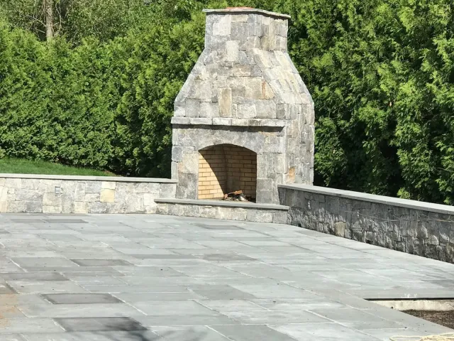 Custom natural stone outdoor fireplace and retaining wall with a bluestone patio — MRO Landscaping project
