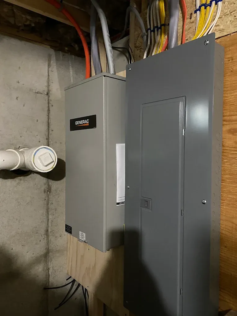 Main electrical panel next to an automatic transfer switch with neatly run circuit cables in a basement