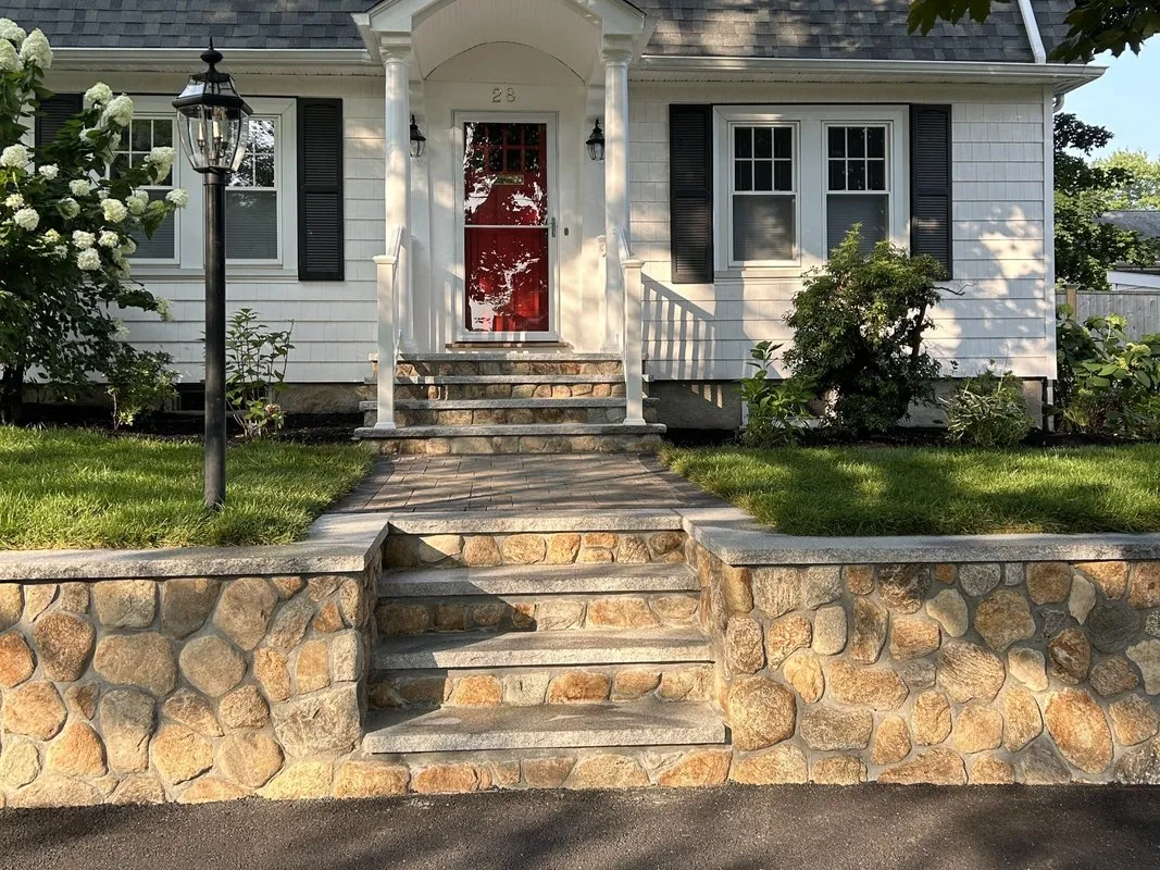 Front yard stone steps and retaining wall in Medford, MA, featuring Boston Blend Round Thin Veneer and granite treads. Designed and built by Goodwood General Construction.