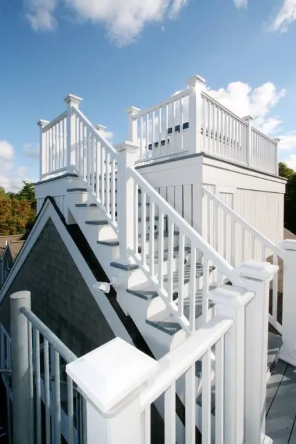 White wooden rooftop deck with stairs and railing, under a partly cloudy sky.