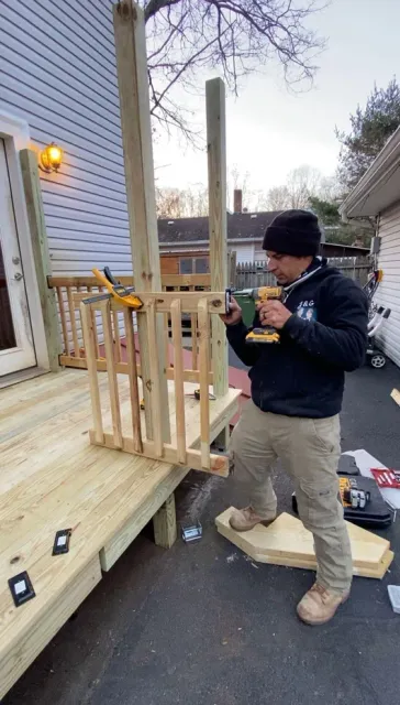 Person assembling a wooden porch railing beside a house, with tools and lumber on the steps