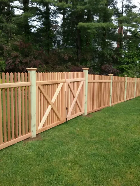 A wooden fence with a gate in the middle of a lush green field.
