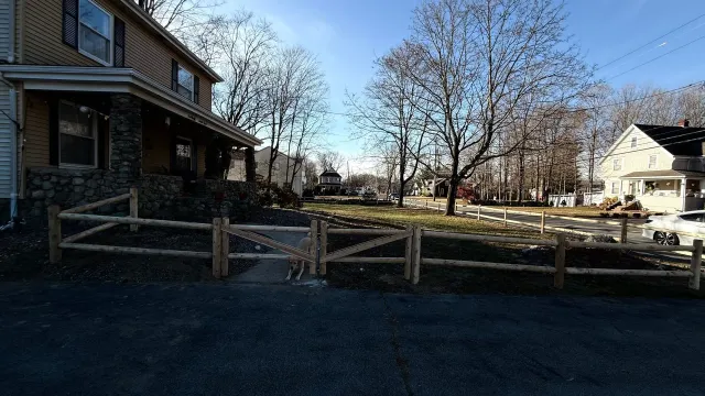 A residential street scene with a wooden fence, houses, and trees on a sunny day.