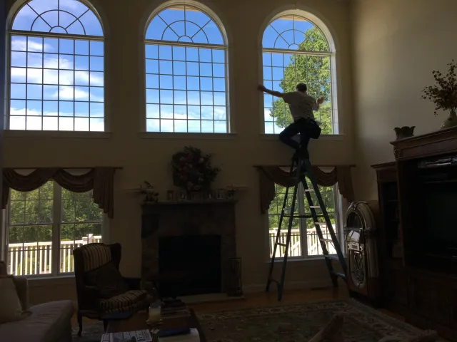 Person cleaning large arched windows in a living room.