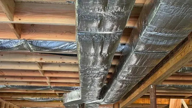 Wooden beams with wrapped, metallic-looking ductwork in a construction setting.