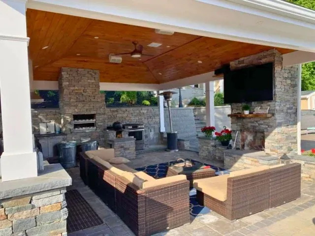 Patio planning for Norfolk & Plymouth County homes: outdoor living area with wood ceiling, stone fireplace, built-in kitchen and wicker seating