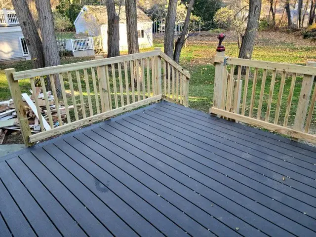 Fresh  deck with light railings overlooking a wooded yard in autumn.