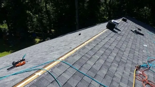 A roof under repair, showing a section of exposed wood ridge vent with new asphalt shingles on both sides.