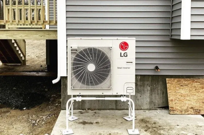 Outdoor air conditioning unit installed on a concrete pad next to a house with gray siding.