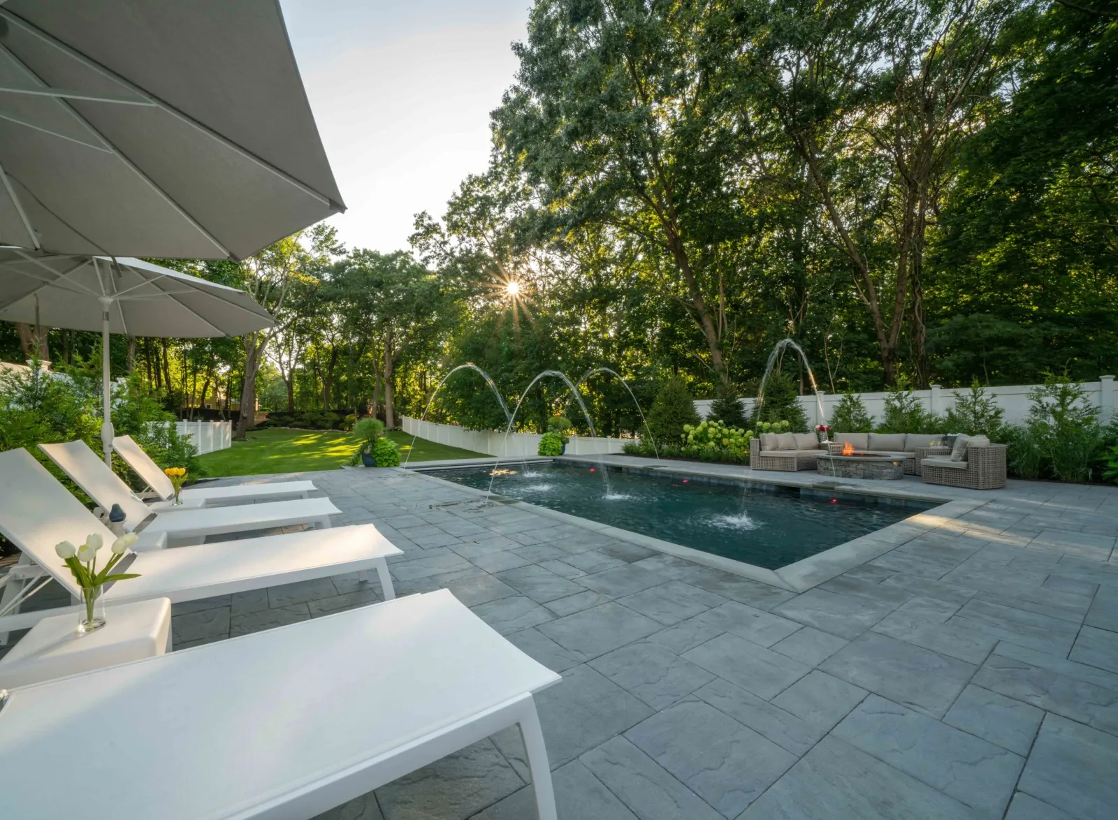 Luxury backyard pool with lounge chairs, fire pit, and water features in Westwood, Massachusetts, designed by Land Design Associates.