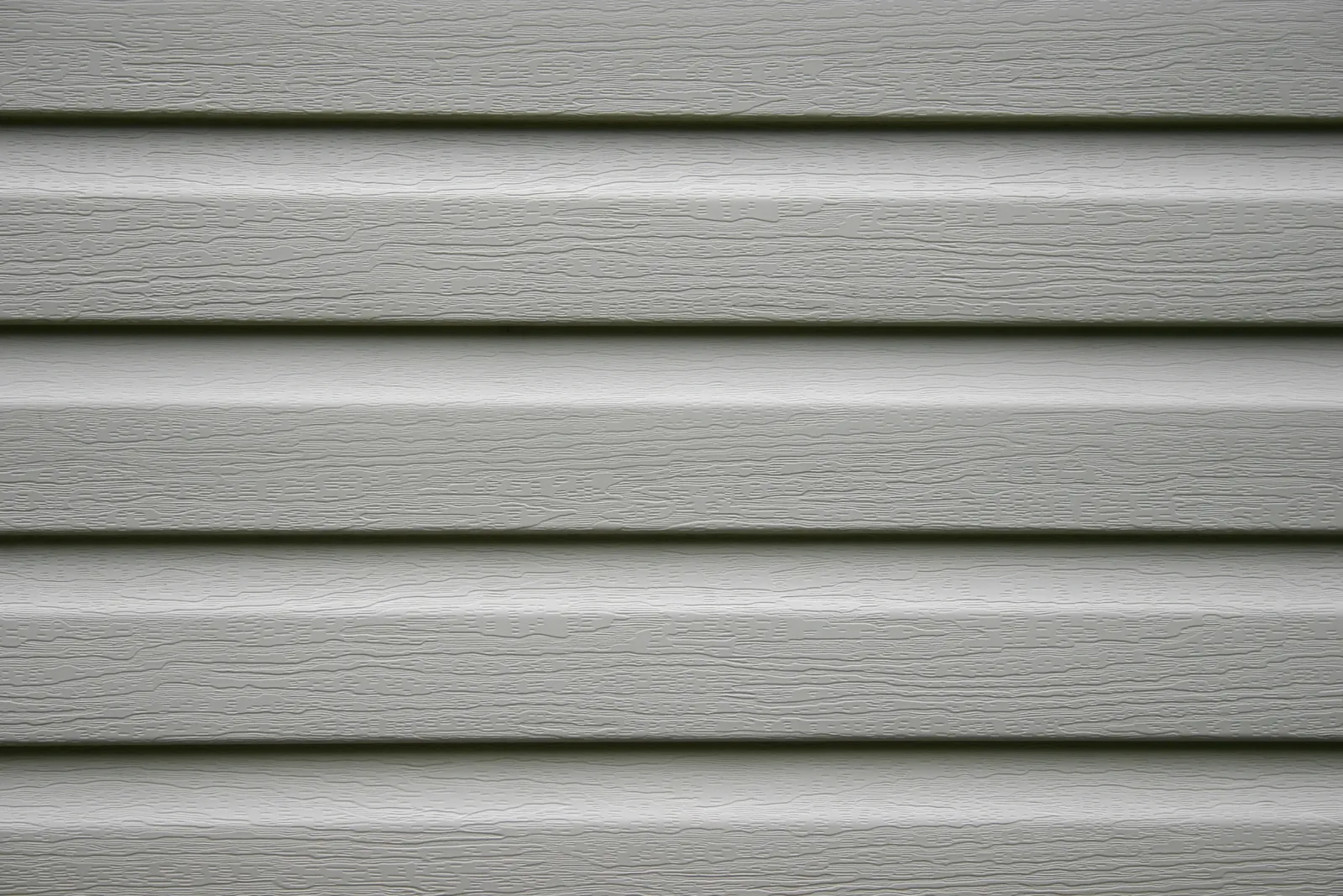 Close-up of gray vinyl siding with wood grain texture.