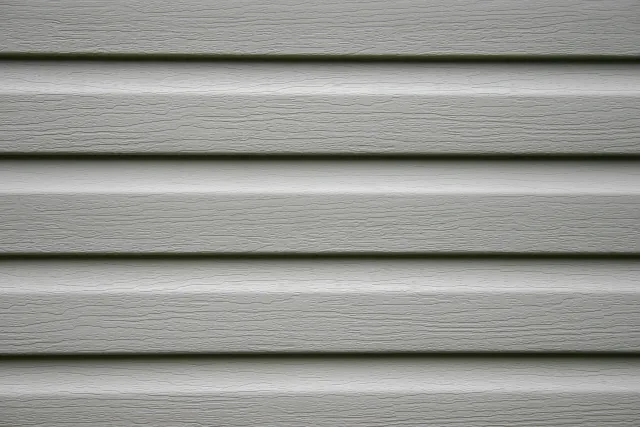 Close-up of gray vinyl siding with wood grain texture.