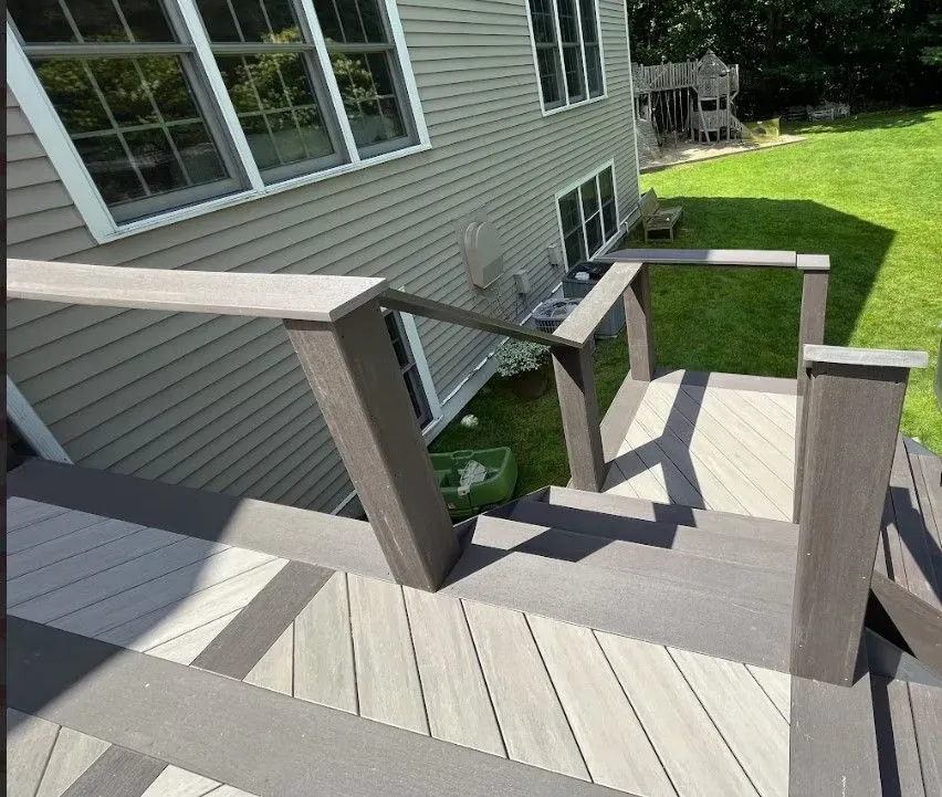 Deck with steps, railing, and house. Gray composite deck and siding. Sunny day.